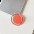 Close-up of a circular orange magnetic phone grip on a modern desk setup - Coral
