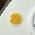 Close-up of a glossy yellow resin phone grip with black stone details on a white tray - Turmeric