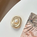 Close-up of golden wavy metal phone grip with a central pearl on a white surface - Transparent Pearl Swirl Style / Matte Gold