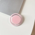 Close-up of a minimalist round magnetic phone grip in sakura pink on a desk edge - Pink