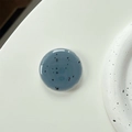 Detail view of round blue-gray phone grip with black speckled texture on white background - Blue Grey