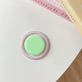 Detail shot of a pastel green and pink collapsible phone grip on a white minimalist desk - Green + Pink