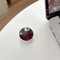 Detailed view of deep brownish-red round phone grip on white desk with laptop - Black