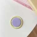 Flat lay of a pastel lavender and yellow round phone socket grip on a white desk - Purple+Yellow