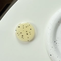 Close-up of minimalist beige resin phone grip with black flecks on a white surface - Milky Yellow