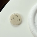Macro detail of glossy cream-colored round phone grip with minimalist black speckles - Milky Grey