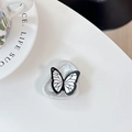 Detalle de un soporte de móvil de mariposa blanca y negra con base de corazón perlado en mesa - Soporte de Anillo Irregular-Textura de Papel de Aluminio-Mariposa de Línea Negra