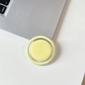 Macro shot of a yellow magnetic Magsafe phone stand on a white desk with laptop - Milky Yellow