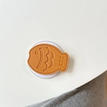 Macro view of orange fish-shaped leather phone grip with detailed lychee grain texture - Golden Brown