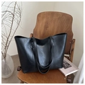 Detail einer schwarzen Leder-Tote-Bag mit Goldschrift auf einem Vintage-Holzstuhl - Schwarz