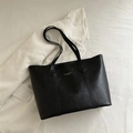Minimalist black faux leather tote bag with gold lettering shown on white textured fabric - Black