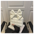 Close-up of cream quilted handbag featuring a large bow handle and soft padded texture - White