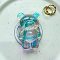 Detailed view of an iridescent bear-shaped magnetic phone grip on a white ceramic plate - Magnetic Bear - Blue Light