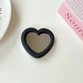 Makroaufnahme von herzförmigem Handy-Griffspiegel mit schwarzem Rahmen auf weißem Tisch - Schwarz
