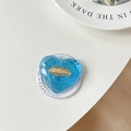 Close-up of heart-shaped blue resin phone grip with silver glitter and gold logo detail - Blue