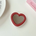 Close-up of red heart phone grip with mirror and matte leather texture on white desk - Burgundy