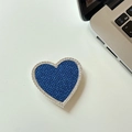 Detail eines funkelnden Herz-Handyhalters mit blauen und weißen Steinen auf dem Tisch - Blau