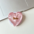 Close-up of pink heart-shaped MagSafe phone grip with gold Smile lettering on a laptop - Magnetic Large Crooked Heart Glitter Gold Smile / Red