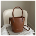 Detail of a brown bucket bag with silver Fashion logo, top handles and thin strap - Tan