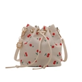 Elegant white bucket bag with red cherry prints and golden hardware in a studio shot - Cherry