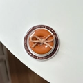 Detail view of a magnetic phone grip button with a plush bow and Gift For You text - Magnetic Bow Button / Brown