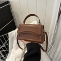 Brown vintage handbag with wave design and gold hardware shown with a white suit - Brown