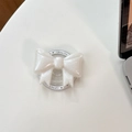 Close-up of a white glittery bow phone socket holder on a minimalist desk background - Magnetic Large Bow - Pearlescent / White