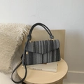 Black and grey striped woven crossbody bag with flap and gold hardware on a table - Black