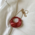 Macro detail of glossy red crescent evening bag with fine textured metallic finish - Red