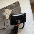 Bolso de hombro retro de cuero negro con elegante cierre giratorio dorado en la mano - Negro