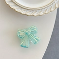 Close-up of an iridescent bow-shaped phone grip with heart detail on a white desk - Iridescent Green