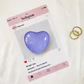 Dettaglio del supporto per telefono a cuore viola in vetro e anelli dorati su carta - Viola