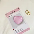 Dettaglio del cuore di vetro rosa e anelli a spirale dorati su carta social media rosa - Rosa Viola