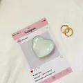 Dettaglio supporto cuore in vetro verde chiaro con due anelli d'oro su una scheda - Verde Latte