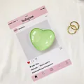 Dettaglio di un supporto per telefono a cuore verde chiaro con anelli in metallo dorato - verde chiaro