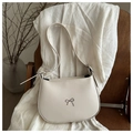 Detalle de bolso de hombro crema con adorno de lazo plateado en silla de madera - Blanco