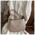 Detalle del bolso de hombro beige claro con lazo metálico plateado en silla de madera - Caqui