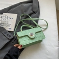 Mint green quilted crossbody bag with a floral lock placed on a stylish grey blazer - Green