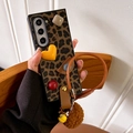 Detail of leopard print folding phone case with 3D charms, wrist strap, and plush pompom - Leopard Geometric Brown Lanyard / Samsung ZFlip3