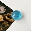 Detailed view of a blue translucent crystal ball phone stand on a white surface - Transparent Blue