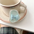 Detail eines hellblauen Bogen-Handyhalters mit silbernem Rahmen auf einer Untertasse - Irisierende Schleife - Perlmuttblau