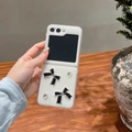 Close-up of white folding phone case with black bows and crystals in hand - Matte Hard Shell-White Glitter Drip-Rhinestone Black Bow / Samsung ZFlip3