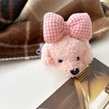 Gros plan du clip téléphone chiot en peluche rose avec noeud sur fond à carreaux - Chien Rose Frisé en Peluche - Nœud Rose à Carreaux