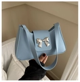 Close-up of light blue leather shoulder bag with a silver metal bow accent - Blue