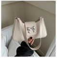 Détail d'un sac selle crème élégant avec une boucle nœud argentée et une bandoulière fine - Blanc