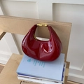 Elegante bolso de media luna en charol burdeos con detalles dorados en una mesa - Rojo