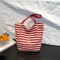 Gestreifte Canvas-Einkaufstasche mit roten Griffen und Handmade-Metallschild auf Steinhintergrund - Rot