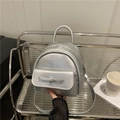 Silberner Mini-Rucksack mit Schleife auf Regal neben Kaffeetassen und Büchern gezeigt - Silber