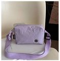 Macro detail of lavender nylon messenger bag featuring metallic logo and fabric texture - Purple