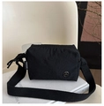 Detail of black nylon crossbody bag with wide strap and metallic M logo on white background - Black